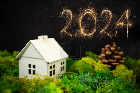 Téléchargez les photos : 2024 écrit avec des spaklers, Modèle maison blanche sur lichen vert ou mousse avec un cône de pin, créatif nouvelle année composition soft focus - en image libre de droit