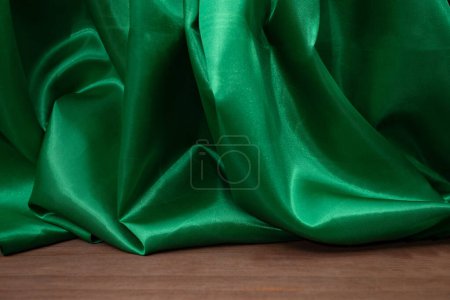 Plancher en bois vide avec des rideaux en tissu satiné vert ondulé élégant, déconcentré en arrière-plan, fond de placement de produit