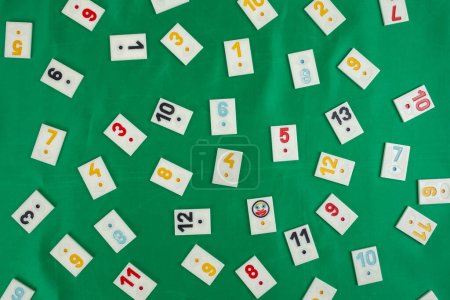 Plastic tiles from the game rummikub, rummy or  okey in Turkey , scattered and arranged on  green background 