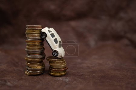miniature white model car leaning on a stack of coins on dark brown leather background, abstract concept, close up