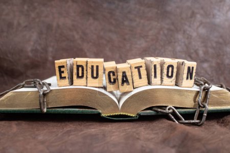 Bildungswort weiß mit Stempelbuchstaben auf Holzklötzen, auf einem aufgeschlagenen Buch mit zerbrochenen Ketten, das das Bildungskonzept repräsentiert