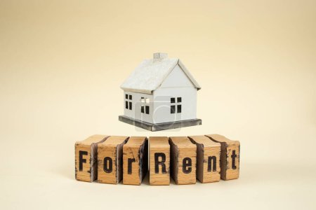 Miniature model house levitating over wooden stamp letters with for rent written text
