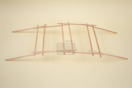 Estructura autoportante para un puente explicado con palos de bambú sobre fondo beige 