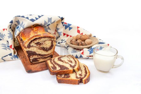 Cozonac, Romanian traditional sweet bread with walnut filling, sliced , with a glass of milk and patterned cloth, side view isolated