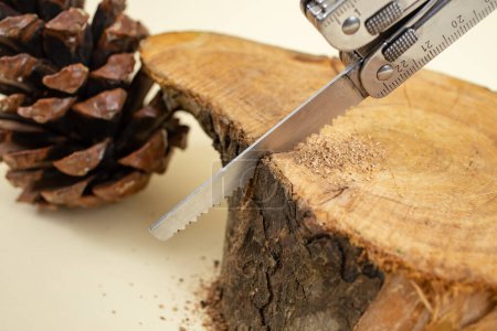 Photo for Swiss army pocket knife sawing a wooden log on beige background, soft focus - Royalty Free Image
