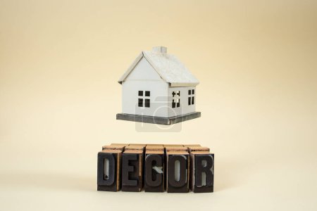 Schwebendes Hausmodell Miniatur über Dekor-Wort geschrieben mit Stempelbuchstaben auf beige 