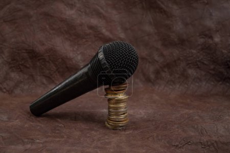 Microphone on a stack of coins on brown leather background, podcast revenue concept 