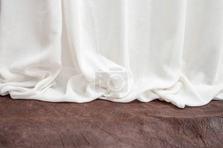 Weiße Stoffvorhänge faltbar auf einer Bühne oder einem Schreibtisch aus braunem Leder 