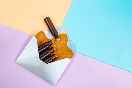 Many essential oil bottles and roll on in a silver envelope with a dried tree leaf on arranged colorful background, abstract alternative medicine backdrop