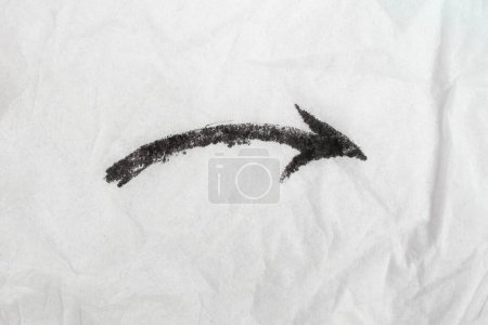 Arrow pointing downward to the right , scribbled with black ink on white crumpled paper  