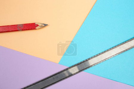 carpentry red crayon with a metal saw blade on colored background 