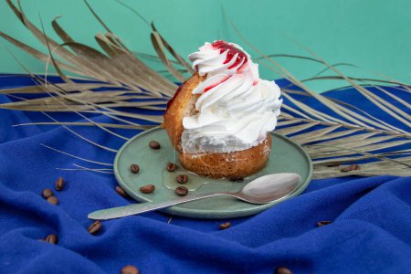 Savarin cake with red glaze and whipped cream on blue cloth  