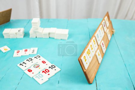 Tuiles en plastique du jeu rummikub, rummicub ou okey en Turquie disposées sur un rack en bois, sur une table bleue 