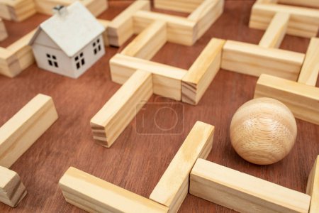 Miniature white house in a wooden maze,  wooden maze made with wood blocks and a wood sphere  finding labyrinth way out concept, soft focus close up 