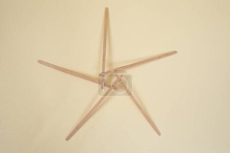 Bamboo wooden sticks demonstrating a pentagram reciprocal frame structure, on beige  