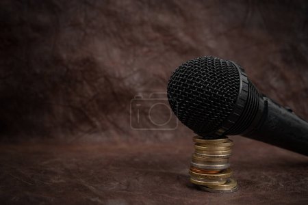 Microphone sur une pile de pièces sur fond cuir marron, concept de recettes podcast 