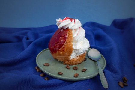 Savarin cake with red glaze and whipped cream on blue cloth  