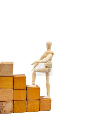 Mannequin en bois grimpant sur escalier en blocs de bois, isolé sur fond blanc 