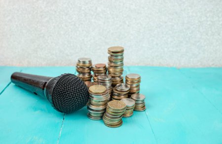 Mikrofon neben Stapeln von Münzen auf blauem Hintergrund, Podcast-Erlöskonzept 