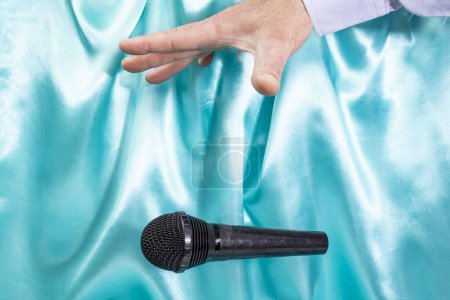 Foto de Caucasian male's hand dropping the mic, stretched hand and a microphone soft focus close up on turquoise satin - Imagen libre de derechos
