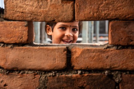 Foto de Una niña india mirando a través de la ventana de la pared de ladrillo de construcción - Imagen libre de derechos