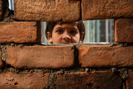 Ein indisches Arbeitermädchen blickt durch ein Ziegelwand-Fenster im Bau