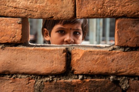 Foto de Una niña india mirando a través de la ventana de la pared de ladrillo de construcción - Imagen libre de derechos