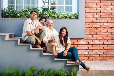 Foto de Retrato de familia india feliz de cuatro sentado al aire libre en las escaleras mirando a la cámara - Imagen libre de derechos