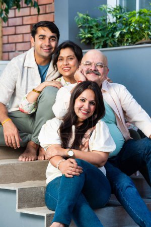 Téléchargez les photos : Portrait de famille indienne heureuse de quatre assis à l'extérieur sur les escaliers regardant la caméra - en image libre de droit