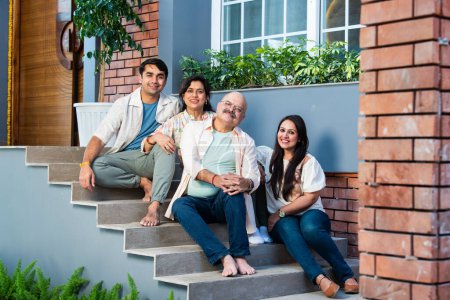 Photo for Portrait of happy Indian family of four sitting outdoor on stairs looking at camera - Royalty Free Image