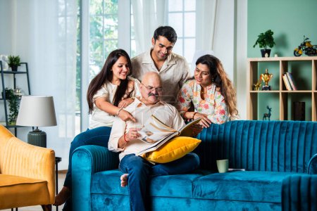 Photo for Indian family looking at Photo album while sitting on sofa, happy moment - Royalty Free Image