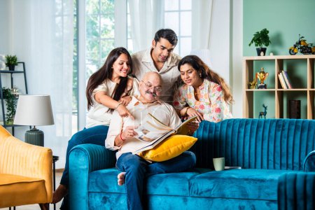 Indische Familie schaut auf Fotoalbum, während sie auf dem Sofa sitzt, glücklicher Moment