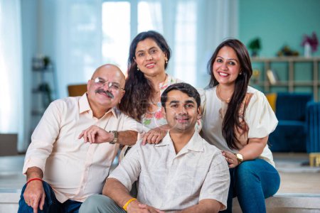 Téléchargez les photos : Famille indienne de quatre personnes posant pour une photo de groupe dans le salon à la maison moderne - en image libre de droit