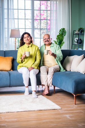Téléchargez les photos : Portrait d'un couple indien âgé assis sur un canapé ou un escalier et prenant un café - en image libre de droit