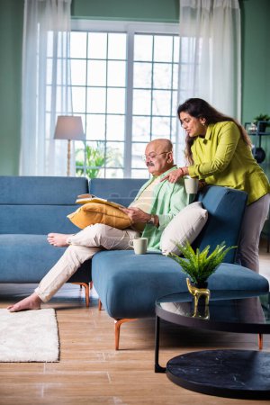 Foto de Riendo pareja india mayor sentado en el sofá en la sala de estar viendo álbum de fotos - Imagen libre de derechos