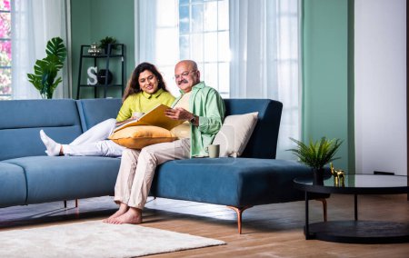 Photo for Laughing senior Indian couple sitting on the couch at living room watching photo album - Royalty Free Image
