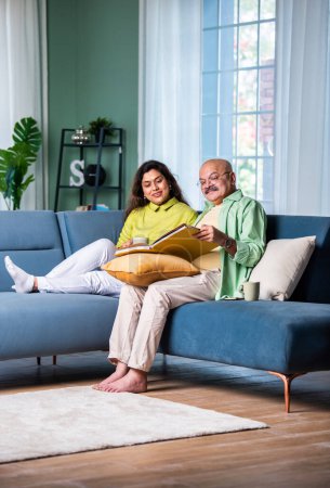 Téléchargez les photos : Rire couple indien âgé assis sur le canapé au salon regarder album photo - en image libre de droit