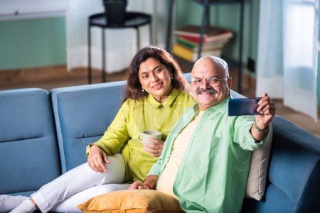 Photo for Happy Senior Indian Couple Using Smartphone Browsing Internet Together Sitting On Couch At Home - Royalty Free Image