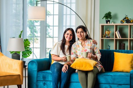 Photo for Mature Indian Mother With Adult Daughter Relaxing On Sofa having coffee At Home - Royalty Free Image