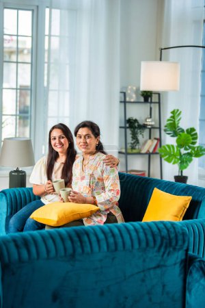 Photo for Mature Indian Mother With Adult Daughter Relaxing On Sofa having coffee At Home - Royalty Free Image