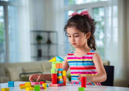 Téléchargez les photos : Petite fille indienne jouant avec des blocs de bois jouets sur la table à la maison - en image libre de droit