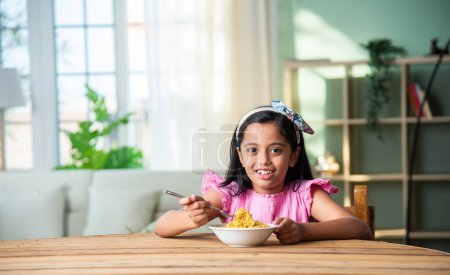 Photo for Indian happy little girl eat pasta spaghetti or noodles in a bowl at home - Royalty Free Image
