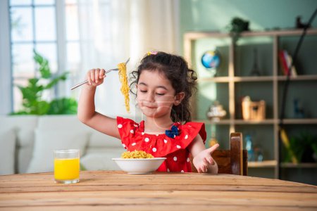 Téléchargez les photos : Indienne heureux petite fille manger pâtes spaghetti ou nouilles dans un bol à la maison - en image libre de droit