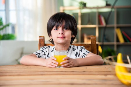 Téléchargez les photos : Indien garçon boire du jus frais dans un verre à la maison - en image libre de droit