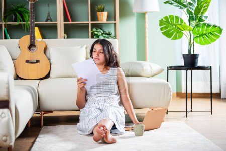 Photo for Indian songwriter girl with paper laptop and guitar at home - Royalty Free Image
