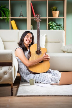 Photo for Indian songwriter girl with paper laptop and guitar at home - Royalty Free Image
