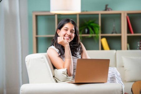 Téléchargez les photos : Indien jeune femme avec un ordinateur portable canapé assis dans un salon moderne - en image libre de droit