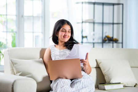 Indian young girl works from home using laptop and documents