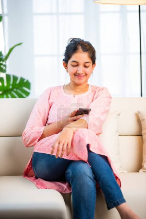 Photo for Indian pretty girl using smartphone for shopping, mesaging in living room - Royalty Free Image