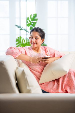 Foto de India bonita chica usando smartphone para ir de compras, mesaging en sala de estar - Imagen libre de derechos